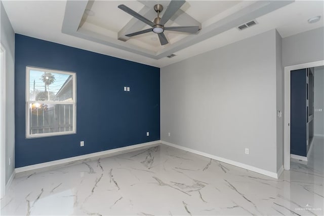 empty room with ceiling fan and a tray ceiling