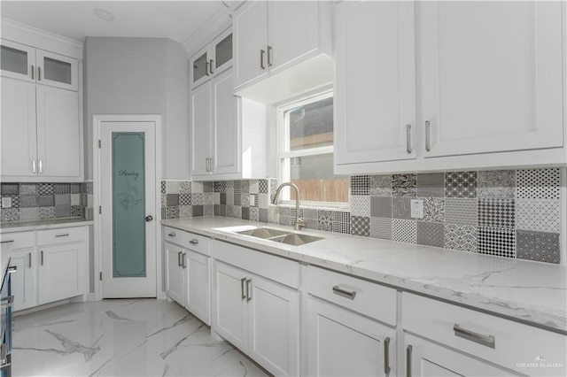 kitchen with light stone countertops, white cabinetry, sink, and tasteful backsplash