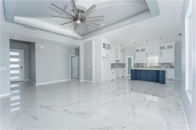 unfurnished living room featuring a raised ceiling, ceiling fan, and sink