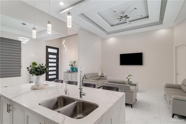 kitchen with open floor plan, a raised ceiling, marble finish floor, and a sink