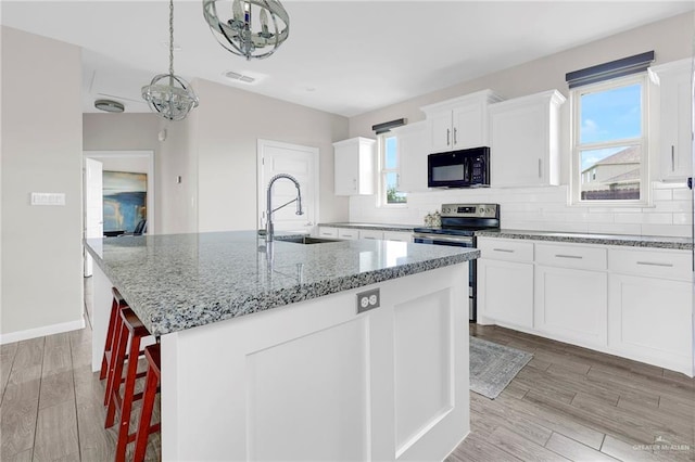 5237 Lost Creek Ln, Mcallen, TX 78504 - kitchen featuring black microwave, stainless steel electric range, a center island with sink, light stone counters, and decorative backsplash
