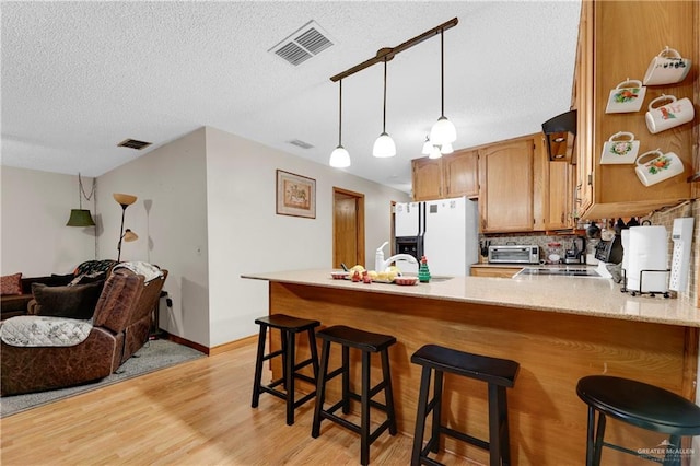 kitchen featuring white fridge with ice dispenser, tasteful backsplash, light hardwood / wood-style floors, kitchen peninsula, and a breakfast bar area