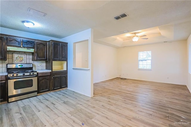 kitchen featuring backsplash, stainless steel range with gas cooktop, ceiling fan, a tray ceiling, and light hardwood / wood-style floors