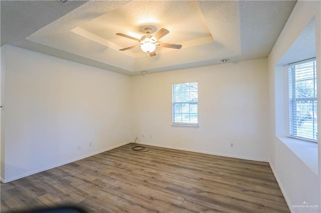 empty room with a tray ceiling, a wealth of natural light, and hardwood / wood-style flooring