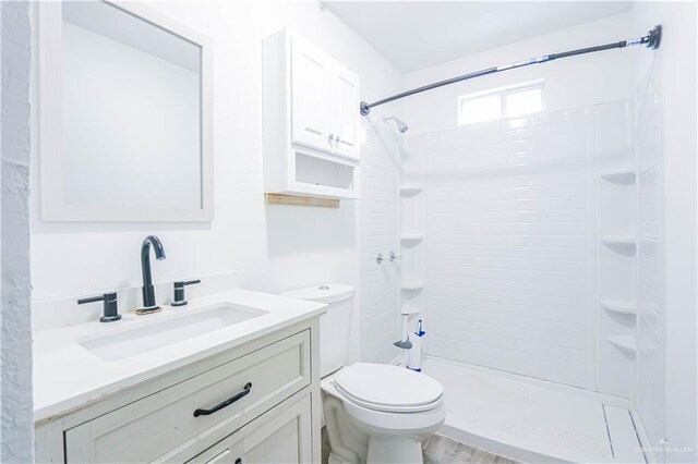 bathroom with hardwood / wood-style floors, vanity, toilet, and tiled shower