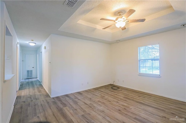 unfurnished room featuring a raised ceiling, ceiling fan, a textured ceiling, and hardwood / wood-style flooring