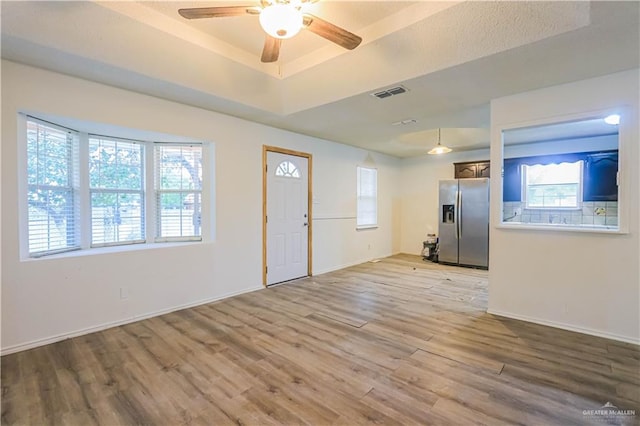 foyer featuring ceiling fan, light wood-type flooring, and a tray ceiling