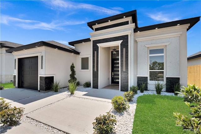 contemporary house featuring stone siding, stucco siding, an attached garage, and fence