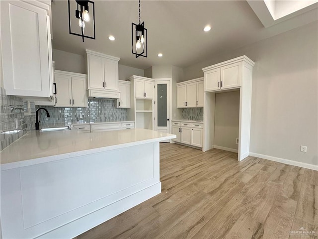 kitchen featuring white cabinetry, sink, pendant lighting, decorative backsplash, and light wood-type flooring