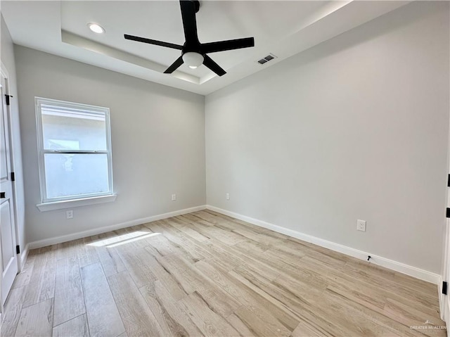 spare room with a raised ceiling, ceiling fan, and light hardwood / wood-style floors