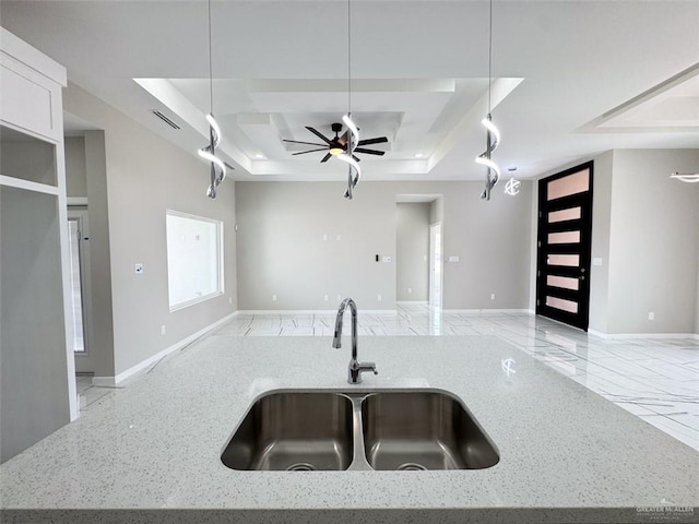 kitchen with light stone counters, sink, a tray ceiling, and an island with sink