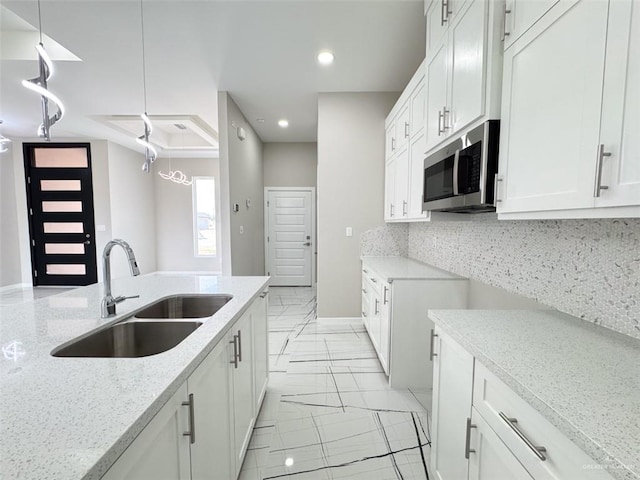 kitchen with sink, hanging light fixtures, tasteful backsplash, light stone countertops, and white cabinets