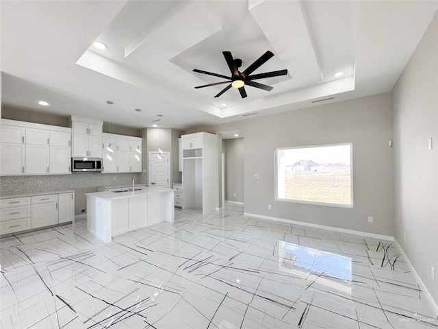 kitchen featuring sink, white cabinetry, a center island with sink, a raised ceiling, and backsplash