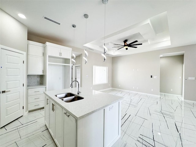 kitchen featuring decorative light fixtures, sink, white cabinets, a kitchen island with sink, and a tray ceiling