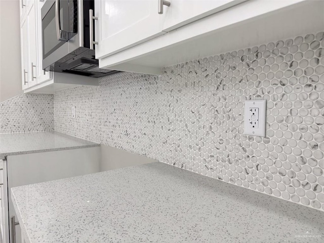 interior details featuring light stone counters, decorative backsplash, and white cabinets