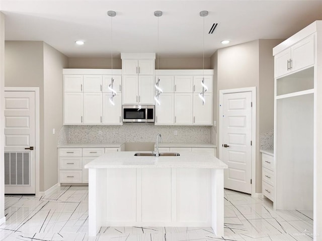 kitchen with decorative light fixtures, sink, a center island with sink, and white cabinets