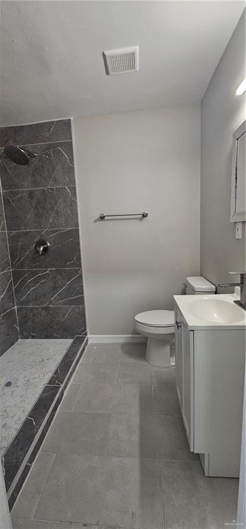 bathroom with tiled shower, vanity, and toilet