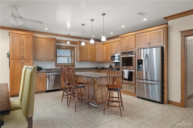 kitchen featuring a center island, ceiling fan, appliances with stainless steel finishes, decorative light fixtures, and a breakfast bar area