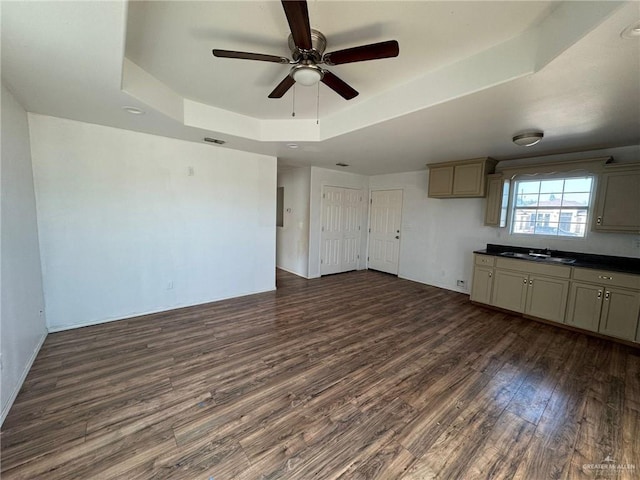 unfurnished living room with dark wood-type flooring, ceiling fan, and a tray ceiling