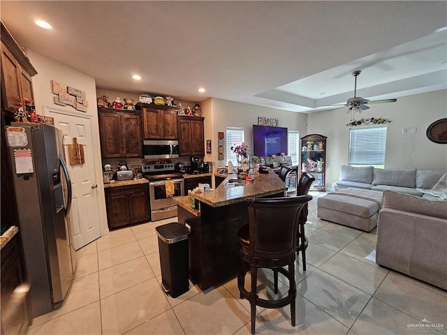 kitchen featuring ceiling fan, a center island, a kitchen breakfast bar, dark brown cabinets, and appliances with stainless steel finishes