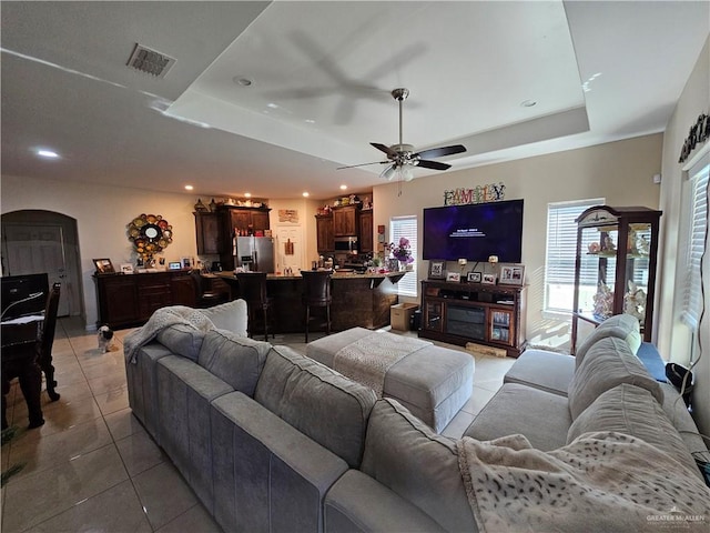 living room featuring ceiling fan, light tile patterned flooring, and a tray ceiling