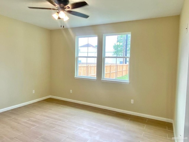 empty room with a healthy amount of sunlight, baseboards, ceiling fan, and light wood-style floors