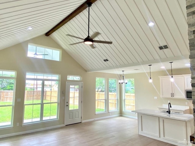 interior space with visible vents, a sink, beamed ceiling, stainless steel microwave, and light wood finished floors