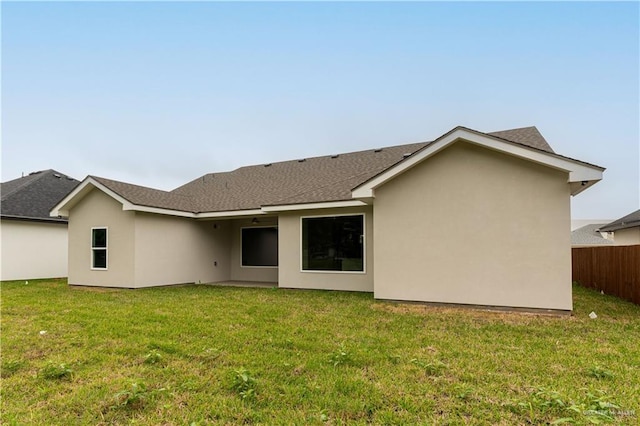 back of property with a lawn, fence, a shingled roof, and stucco siding