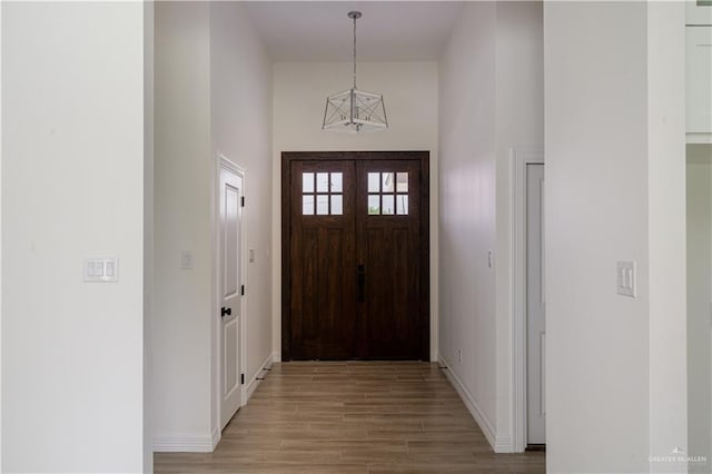 foyer featuring baseboards, light wood finished floors, and a towering ceiling