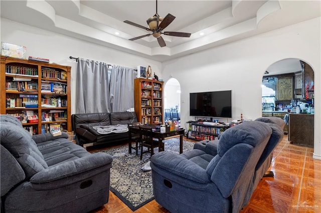 living area featuring arched walkways, a raised ceiling, ceiling fan, wood finished floors, and recessed lighting