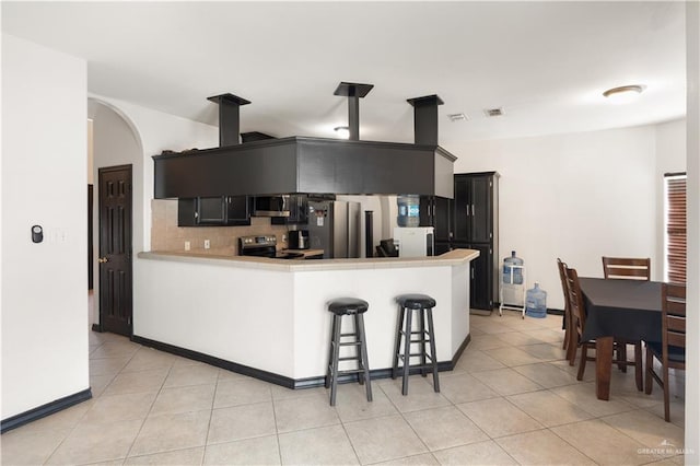 kitchen with kitchen peninsula, tasteful backsplash, a breakfast bar, stainless steel appliances, and light tile patterned floors