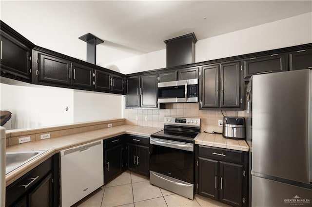 kitchen with tasteful backsplash, stainless steel appliances, sink, light tile patterned floors, and tile counters