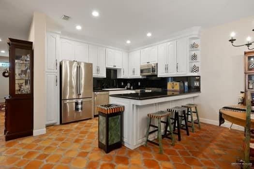 kitchen featuring white cabinetry, stainless steel appliances, kitchen peninsula, a breakfast bar area, and decorative backsplash