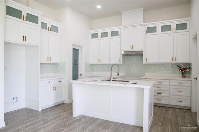 kitchen with glass insert cabinets, light countertops, an island with sink, and white cabinetry