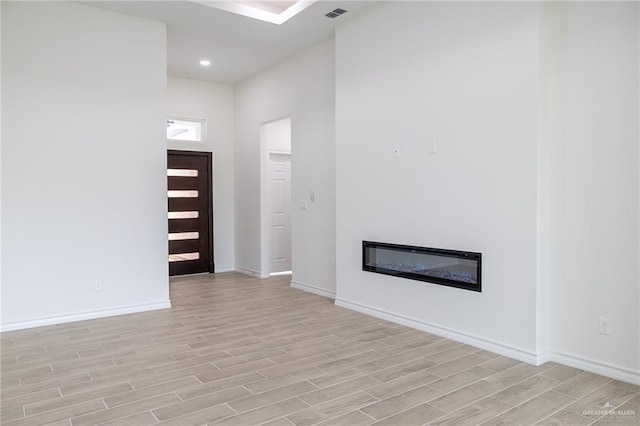 entrance foyer featuring recessed lighting, visible vents, baseboards, light wood-type flooring, and a glass covered fireplace