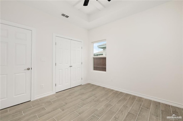 unfurnished bedroom featuring wood finish floors, a ceiling fan, visible vents, baseboards, and a closet