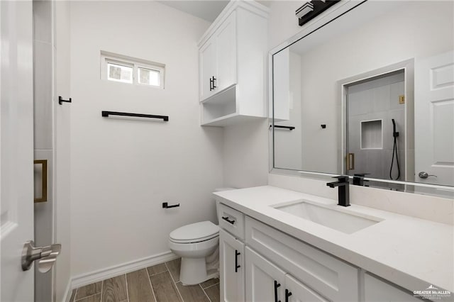 bathroom featuring toilet, wood tiled floor, a shower stall, vanity, and baseboards