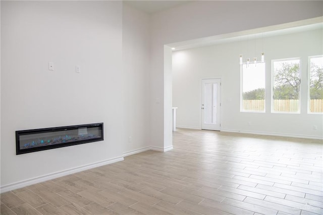 unfurnished living room featuring light wood-type flooring, a glass covered fireplace, and baseboards