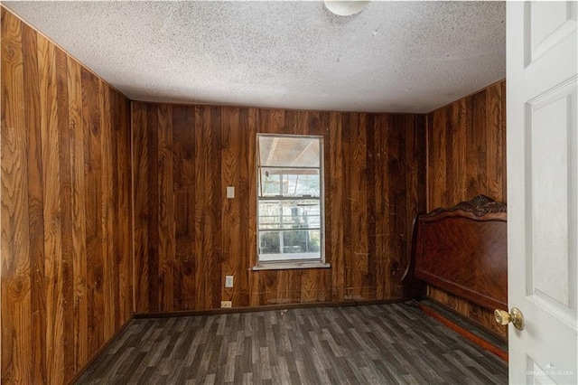 unfurnished room with a textured ceiling, wood finished floors, and wooden walls