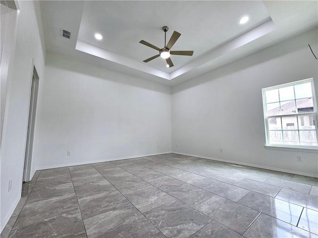 spare room with ceiling fan and a raised ceiling