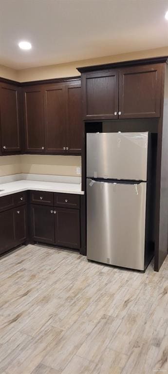 kitchen with stainless steel fridge, dark brown cabinetry, and light hardwood / wood-style floors