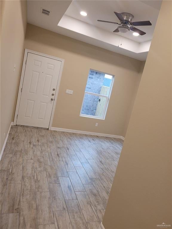 entrance foyer with ceiling fan, light hardwood / wood-style floors, and a tray ceiling