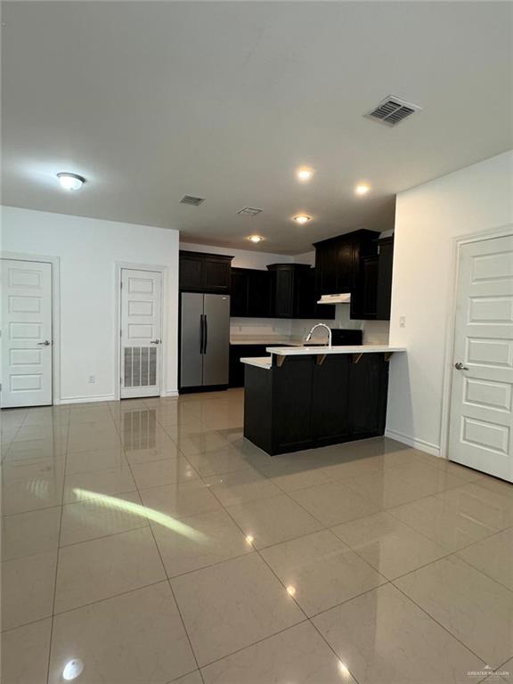 kitchen featuring sink, light tile patterned floors, a kitchen bar, kitchen peninsula, and stainless steel refrigerator