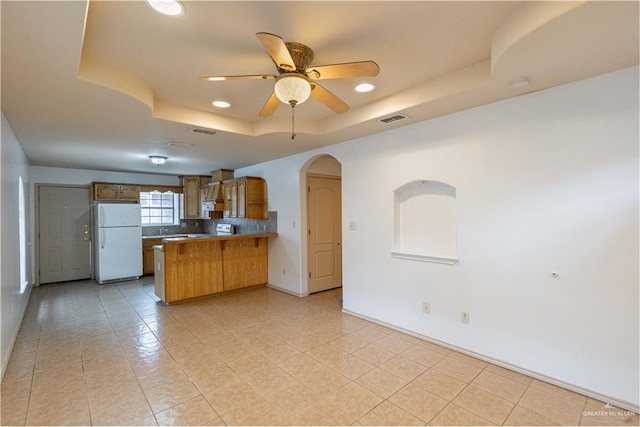 kitchen featuring ceiling fan, white fridge, a raised ceiling, and kitchen peninsula