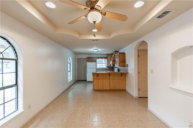 kitchen with kitchen peninsula, a raised ceiling, ceiling fan, white fridge, and light tile patterned flooring