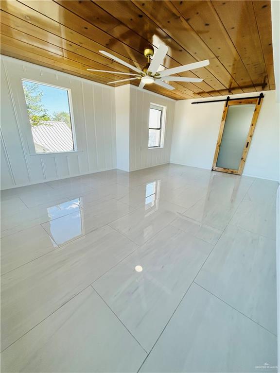 empty room featuring a barn door, wooden ceiling, and ceiling fan