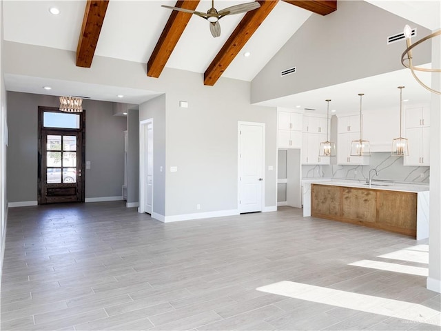 unfurnished living room with baseboards, beamed ceiling, high vaulted ceiling, a ceiling fan, and a sink