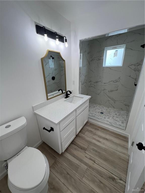 bathroom with a marble finish shower, toilet, vanity, wood finished floors, and baseboards