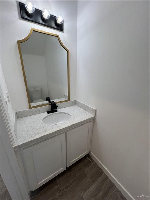 bathroom with baseboards, vanity, toilet, and wood finished floors