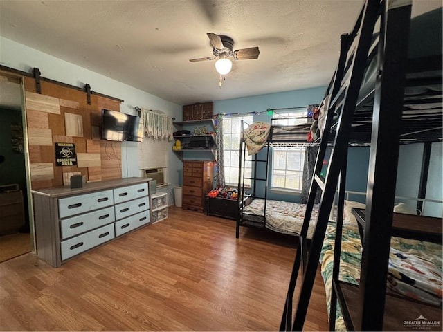 bedroom with a textured ceiling, a barn door, light hardwood / wood-style flooring, and ceiling fan